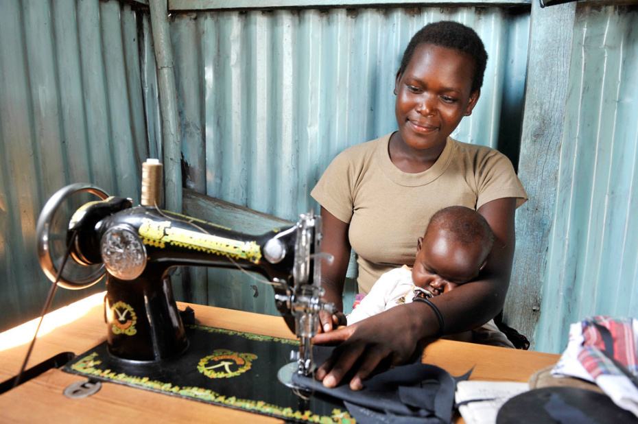 A woman working at a sowing machine, with a child on her lap.