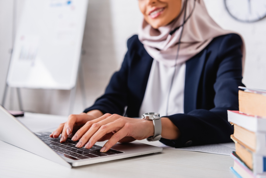 A woman typing on a laptop. She is wearing a headset. The upper part of her face is not seen as to keep her anonymous. 