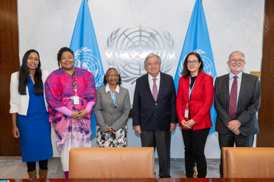 Secretary-General António Guterres (centre right) with five members (4 females and 1 male) of the Coordination Committee of Special Procedures in front of two UN flags and the UN logo.