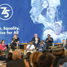 A podium discussion ongoing in front of a backdrop saying "Human Rights 75 - Freedom, Equality and Justice for All"