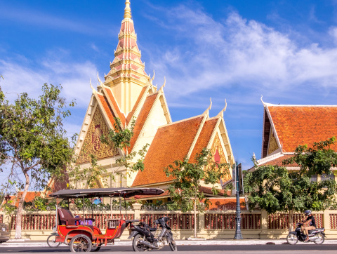 An outside view of the Cambodia Surpreme Court building, with a tuk tuk standing on the road in front of it.