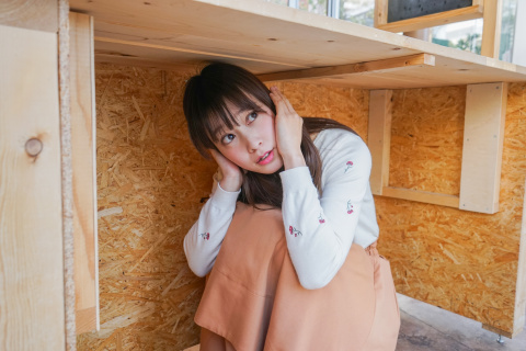 A young woman kneeling under a table, covering her head.