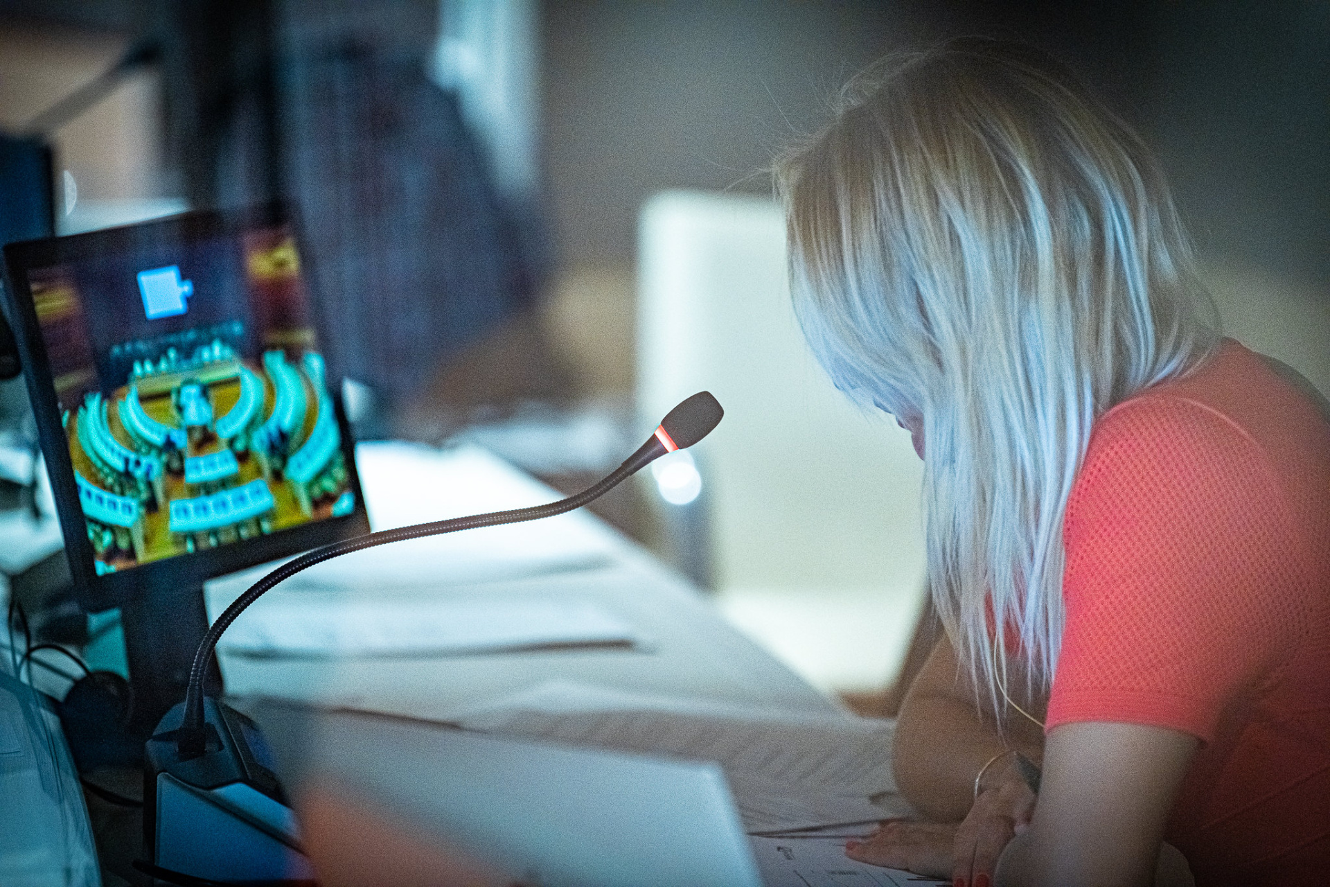 An interpreter speaking into the microphone while following a meeting on a small screen in her cabin. 