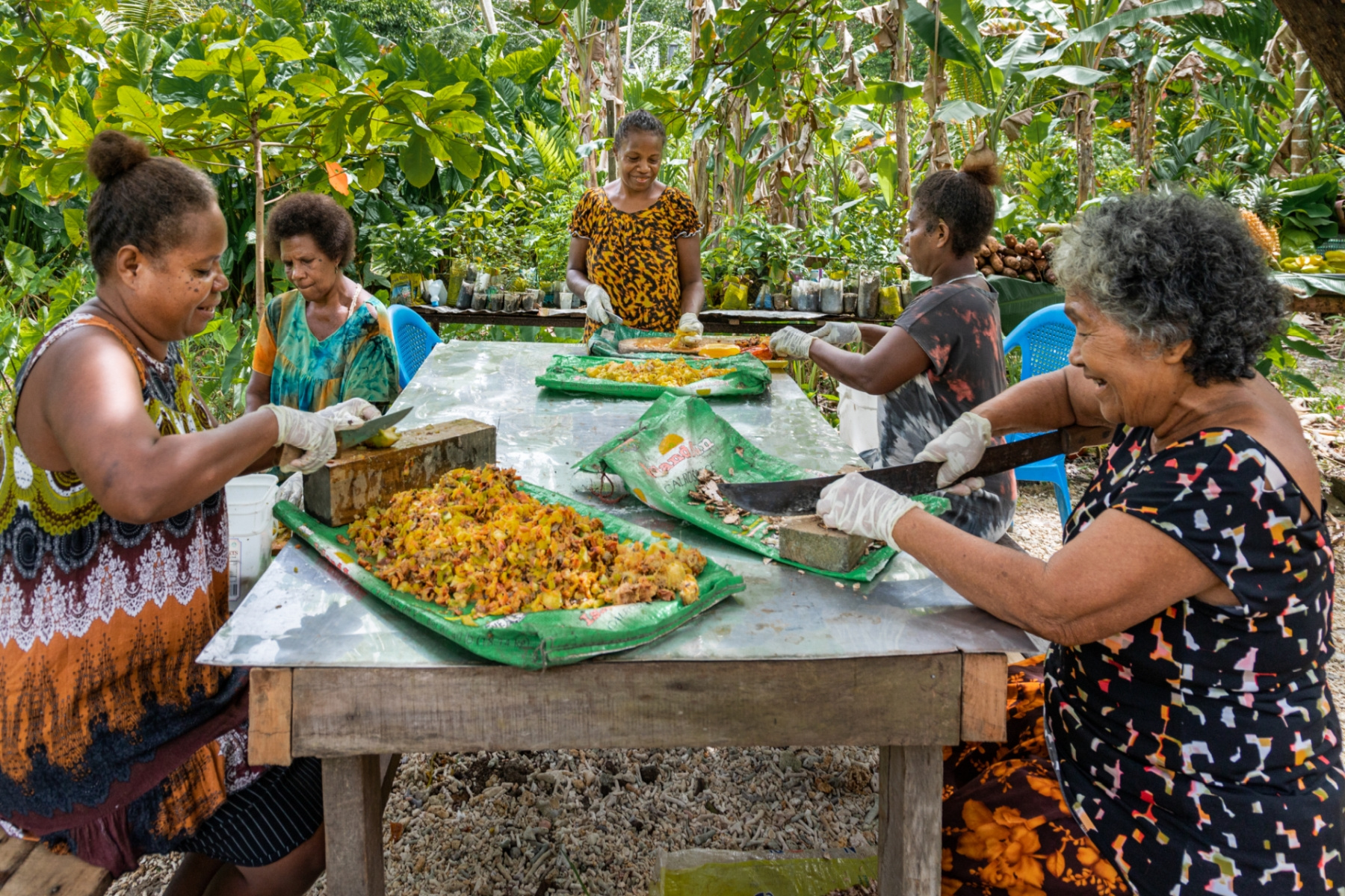 5 women sit outside and prepare food. 