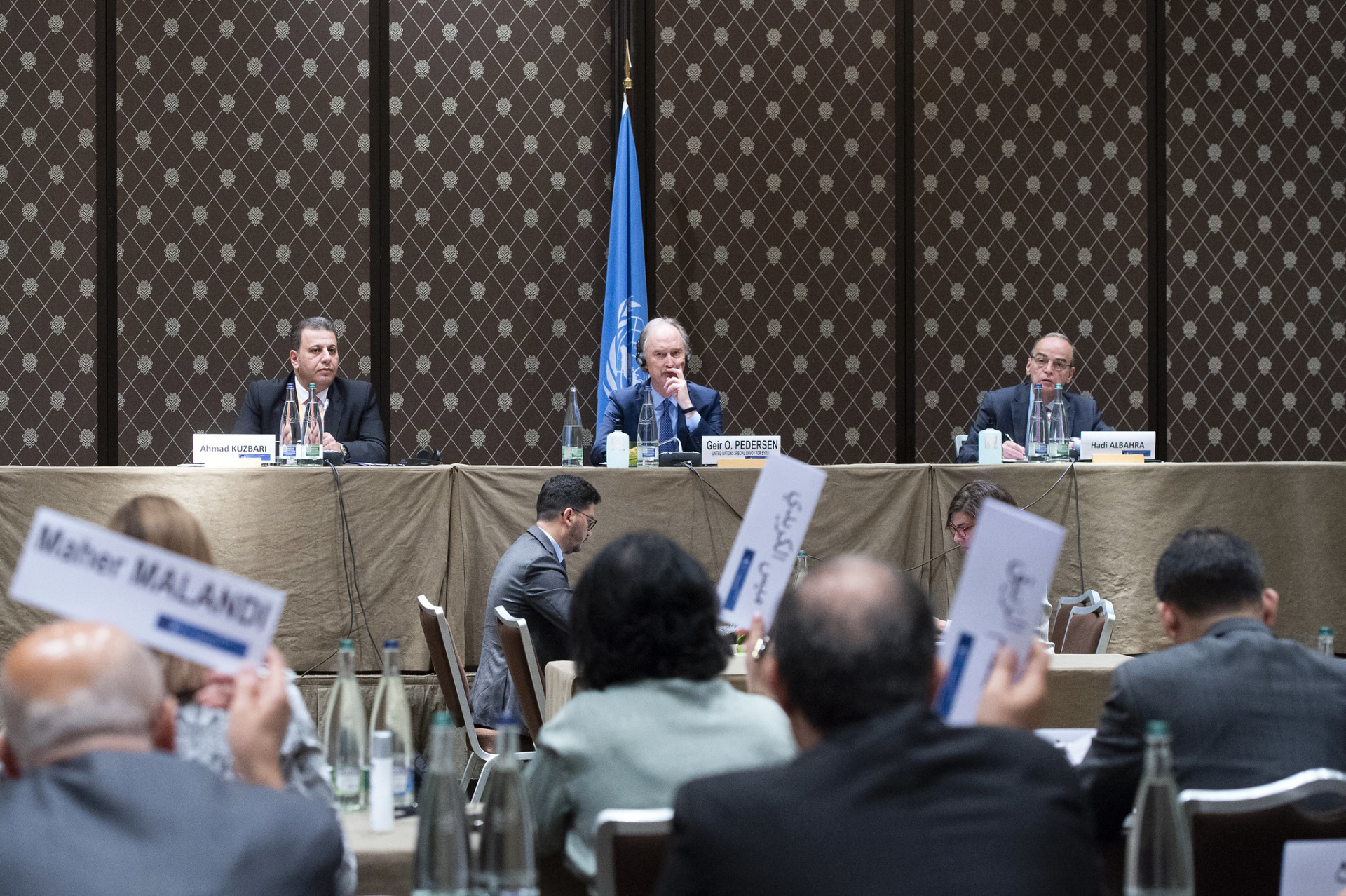 Special Envoy for Syria, Geir O. Pedersen sitting on a podium between a representative of the Syrian Government and one from the opposing Syrian Negotiations Commisssion who form part of the Syrian Constitutional Committee. 