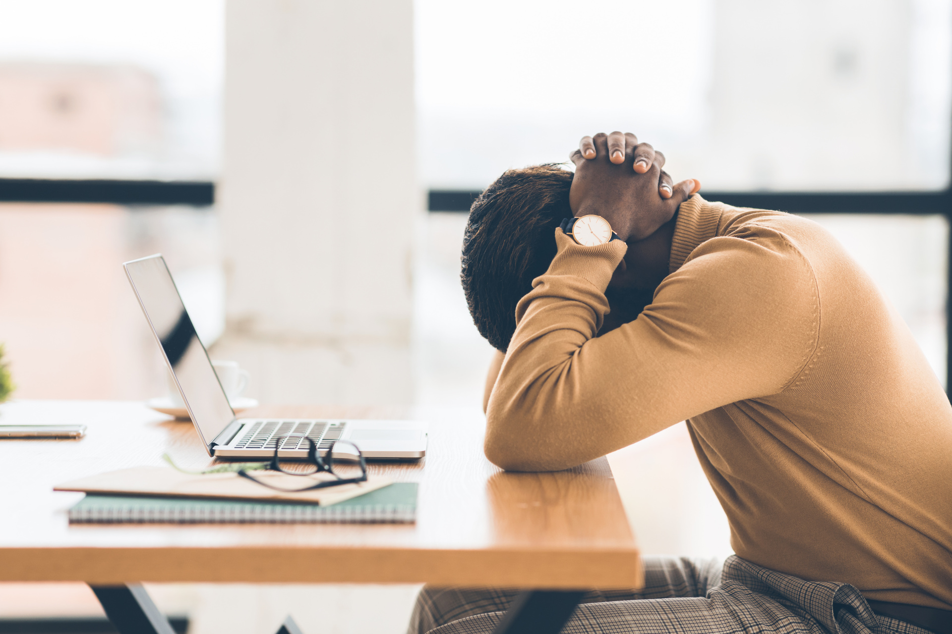 A man sunken down on his desk, in front of his laptop, the head hidden under the arms.