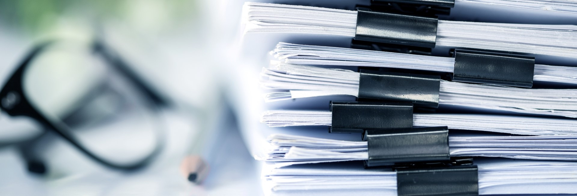 A stack of files next to some reading glasses and a pen.