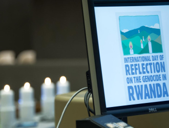 A laptop shows the words "International Day of Reflection on the Genocide in Rwanda". Candles are seen in the background. 