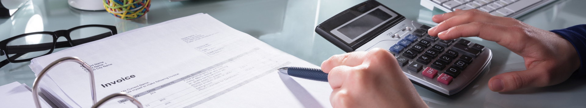 A man is making calculations using documents and a calculator. Only his hands are seen in the image.