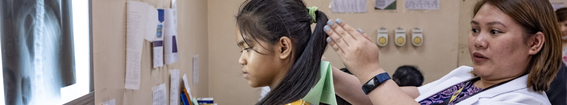 A medical worker examines a girl's head. On the left side, an x-ray image of a thorax is seen.