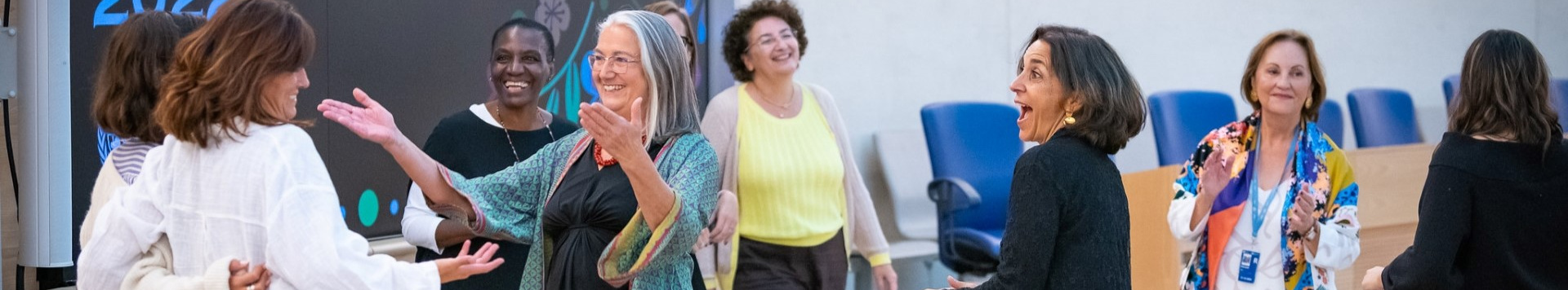 Eight UNOG female staff talk cheerfully in one of the conference rooms